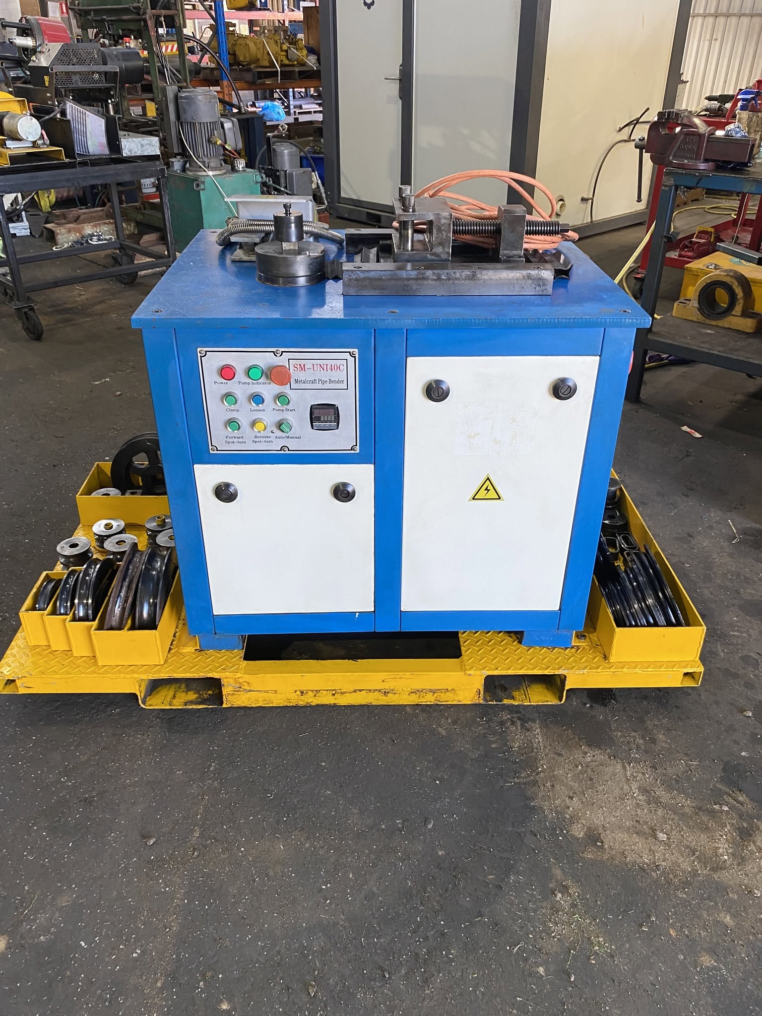 Blue hydraulic pipe bender on a yellow pallet with tooling in trays