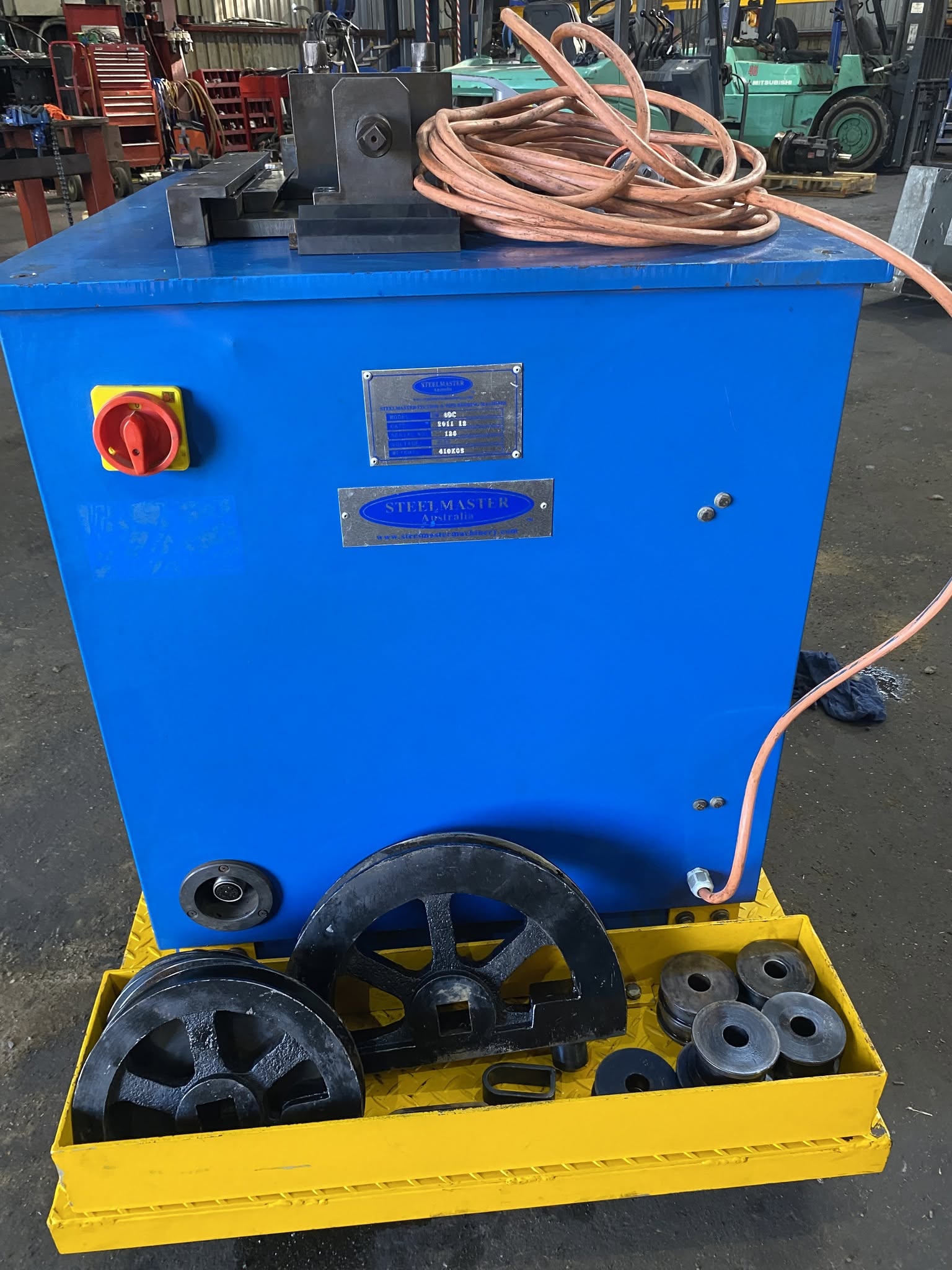 Side view of a blue machine with bending wheels and tooling on a yellow pallet